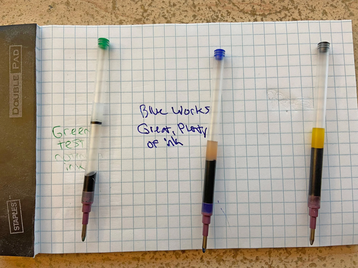 Pen ink refills with green, blue, and black ink tested on grid paper to demonstrate ink quality and color vibrancy.