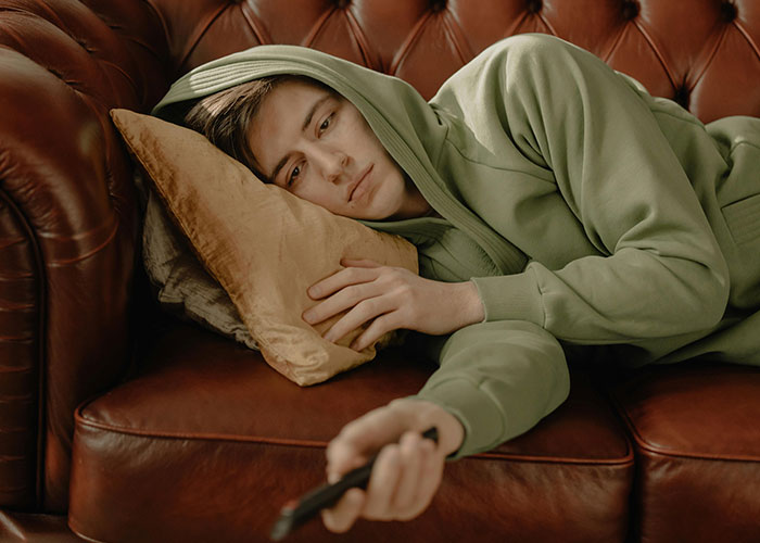 Young person in a green hoodie lying on a leather couch, looking pensive, illustrating neurodivergent experiences.