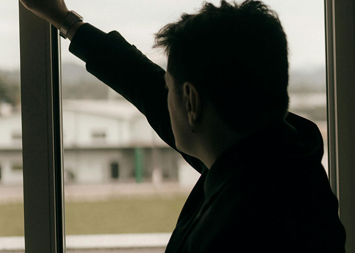 Man looking out window, reflecting on life changes after discovering he wasn’t the biological parent.