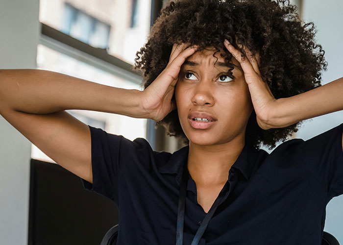 Woman with curly hair holding her head, appearing stressed and overwhelmed, representing neurodivergent experiences.