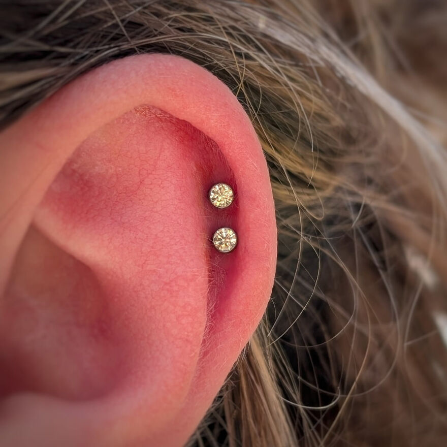 Close-up of an ear with double helix piercing showing two small sparkling stud earrings in the cartilage area.