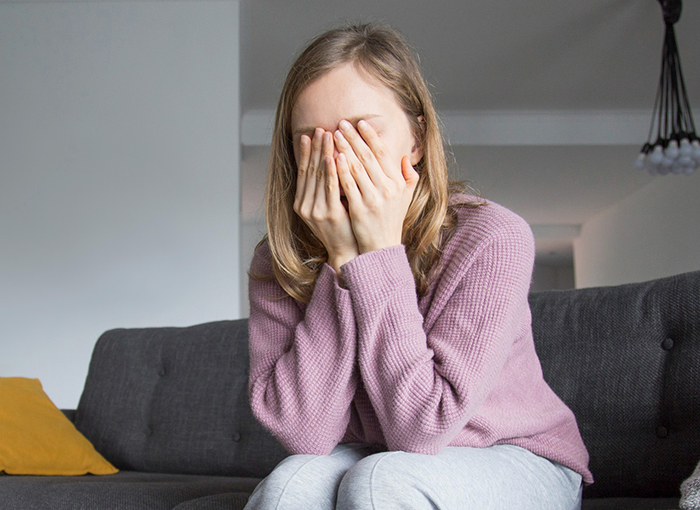 Woman in a purple sweater sitting on a couch covering her face, reflecting fears about golddiggers in a relationship.