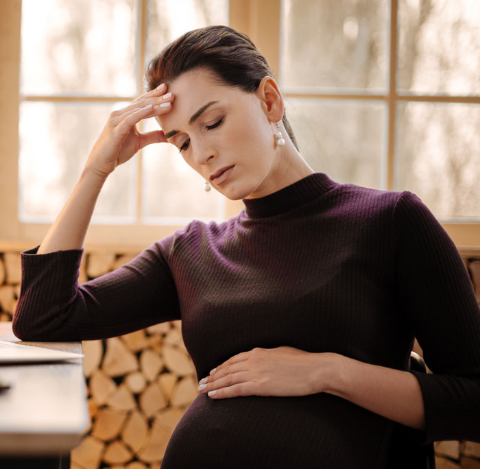 Pregnant woman feeling stressed, holding her belly, worried about fianc&eacute;&rsquo;s mom in delivery room compromise.