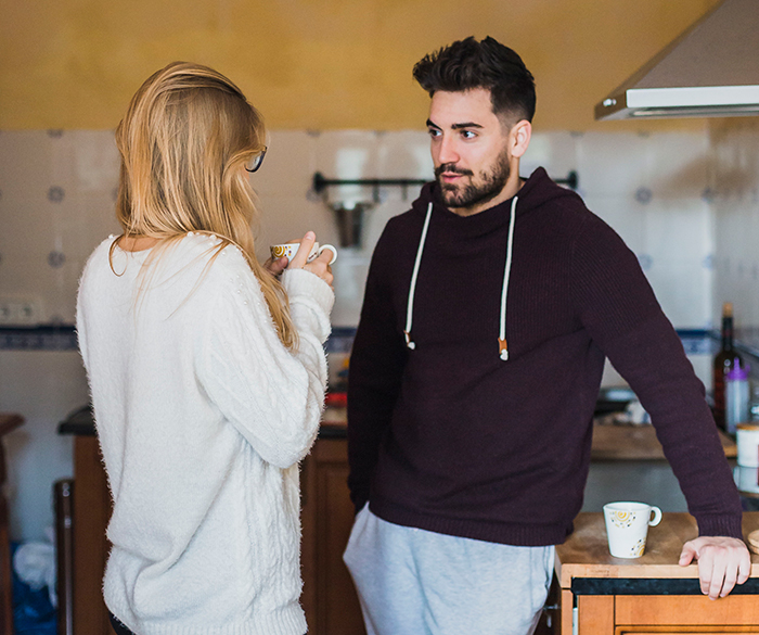 Worried woman talks to man in kitchen, reflecting concern about sister who became a tradwife and secret fund support.