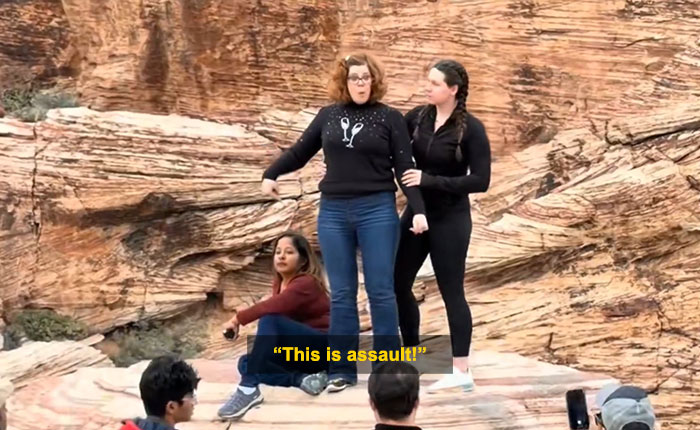 Woman blocks tourist&rsquo;s shot in viral Red Rock Canyon incident with rocky desert background and bystanders nearby.
