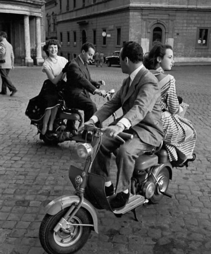 Two couples riding vintage scooters on a cobblestone street, capturing unexpected and beautiful street moments.