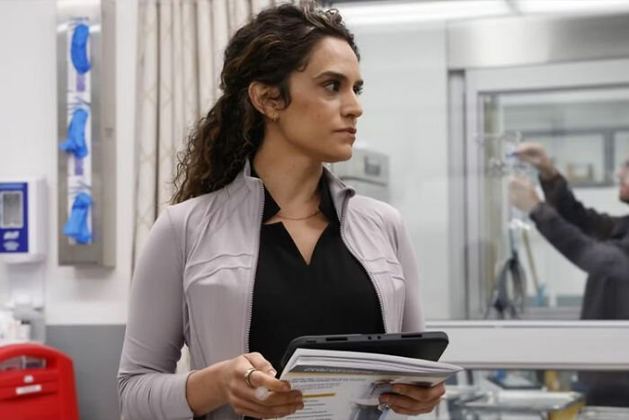 Woman holding documents and tablet in a medical setting, related to The Pitt Season 2 Episode 1 recap highlights.