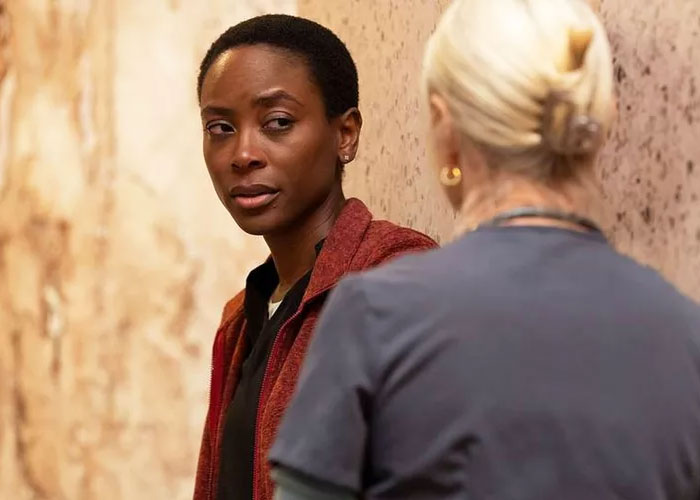 Two women talking in a dimly lit hallway, focusing on Dr. Heather Collins in a serious conversation scene.