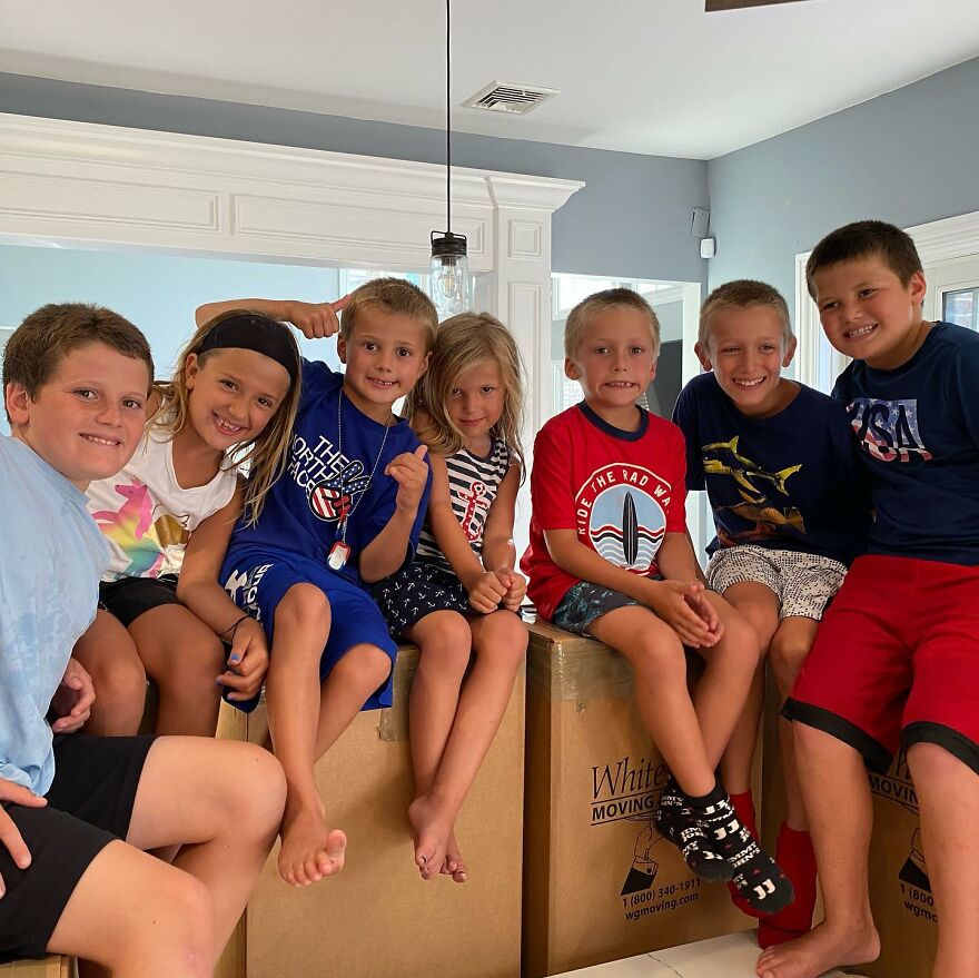Seven smiling children sitting on moving boxes indoors, capturing the challenge of keeping track of Pete Hegseth family.