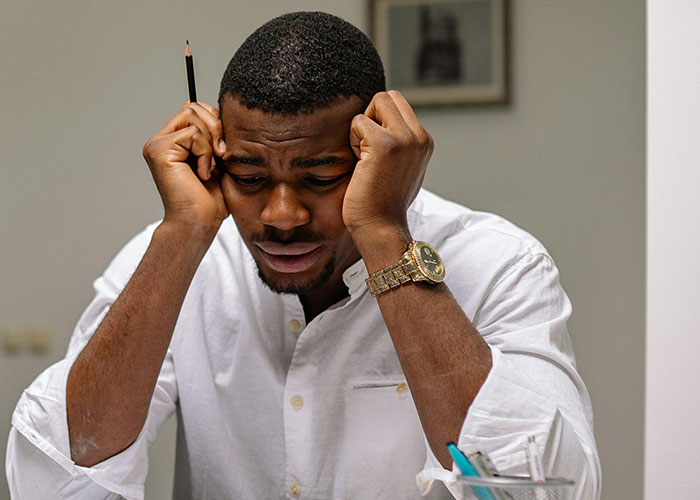 Young man in a white shirt holding a pencil, appearing thoughtful and stressed while reflecting on neurodivergent traits.