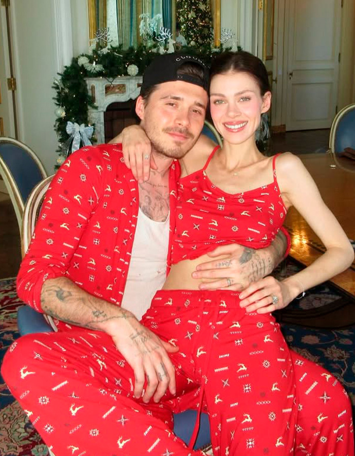 Brooklyn Beckham and wife Nicola wearing matching red outfits, seated in a festive room with Christmas decorations.