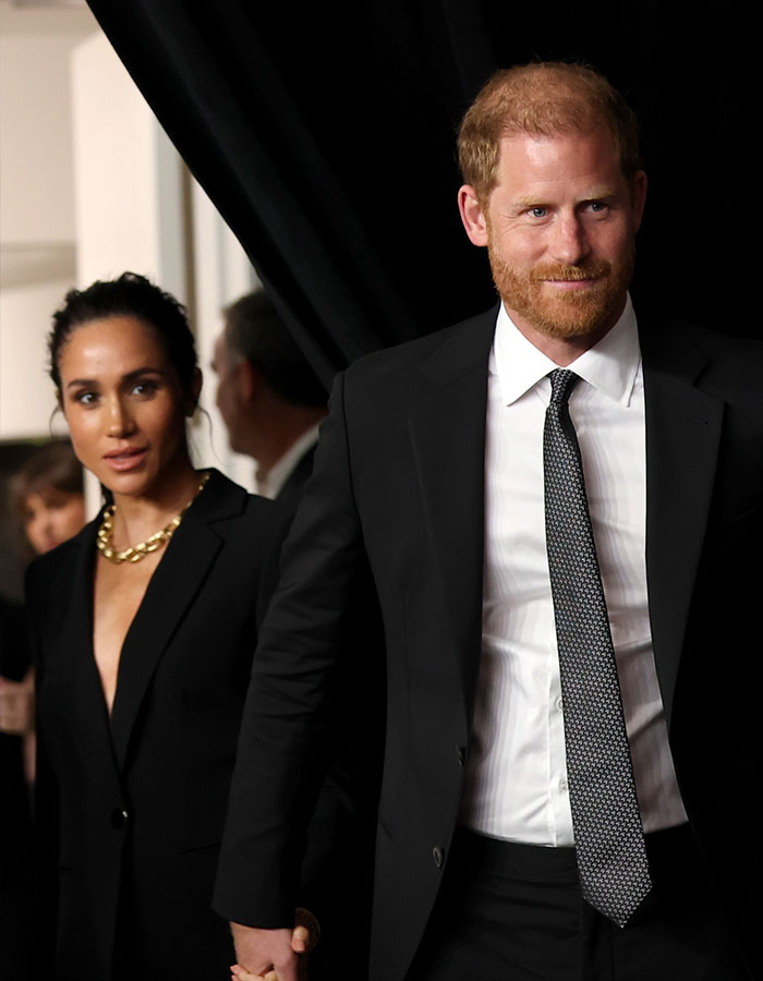 Prince Harry and Meghan Markle dressed formally at an event, with focused expressions and close proximity.