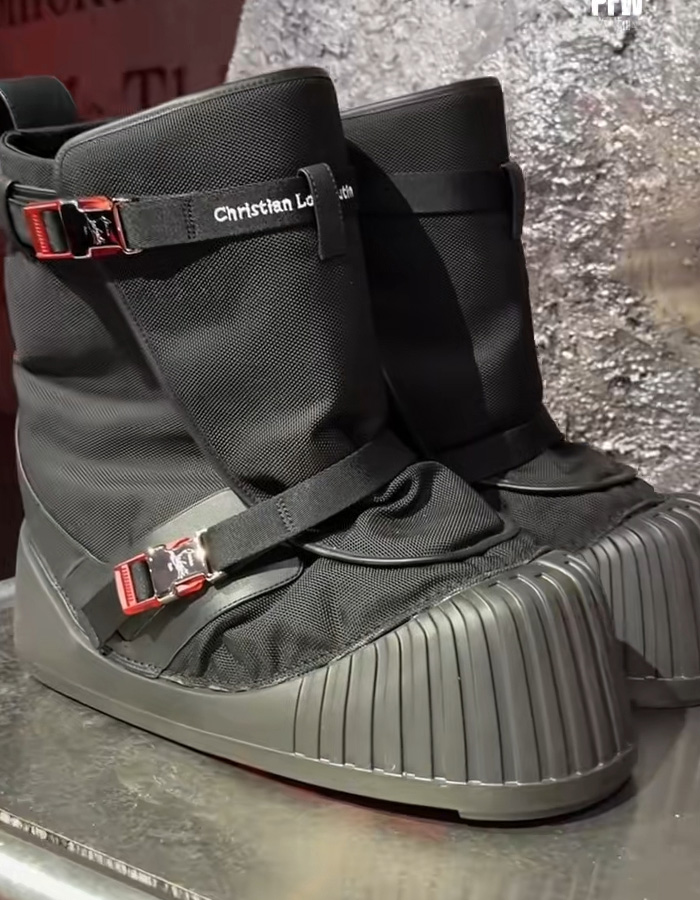 Black Christian Louboutin sneakers with red buckles and textured soles displayed on a metallic surface. Black Christian Louboutin sneakers with red buckles and textured soles displayed on a metallic surface.