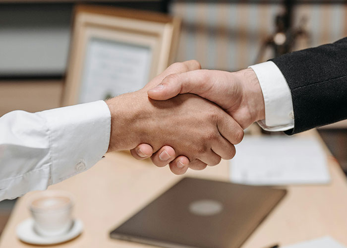 Two people shaking hands in a formal setting, symbolizing perfect revenge acts without getting caught.
