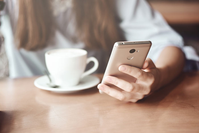 Person holding a smartphone with a cup of coffee nearby, highlighting the role of the phone in cheating revelations.
