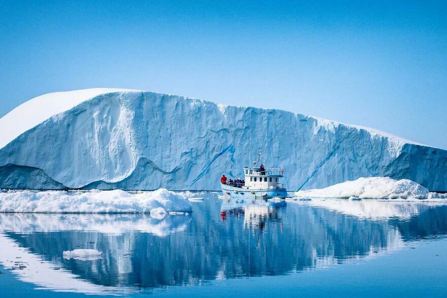 Boat sailing near a massive iceberg in clear blue waters, showcasing one of the places you should visit at least once.