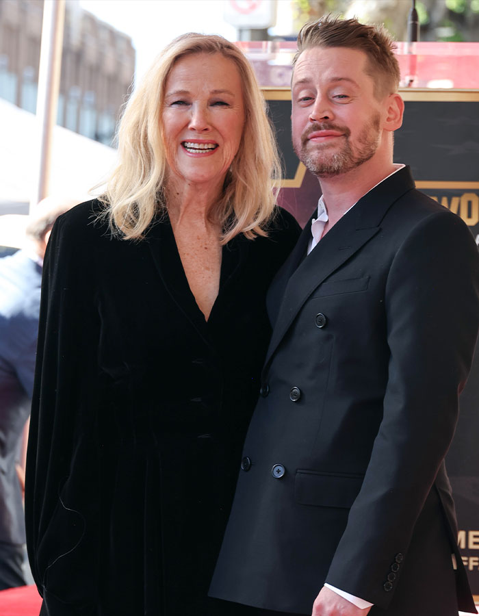Schitt’s Creek star Catherine O'Hara smiling and posing with a man in black suits at an outdoor event. Schitt’s Creek star Catherine O'Hara smiling and posing with a man in black suits at an outdoor event.