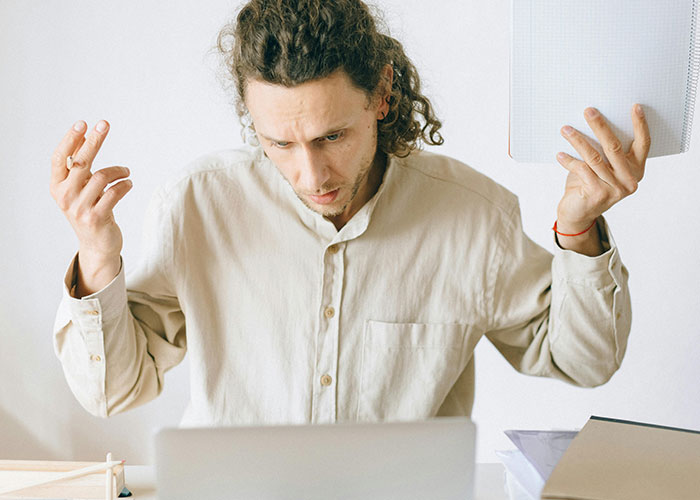 Man with curly hair holding paper looking confused while working on laptop, illustrating neurodivergent experiences.