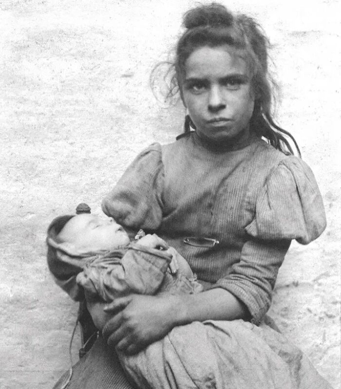 Young girl holding a baby in her arms, depicting a sad and beautiful moment in the history of humanity.