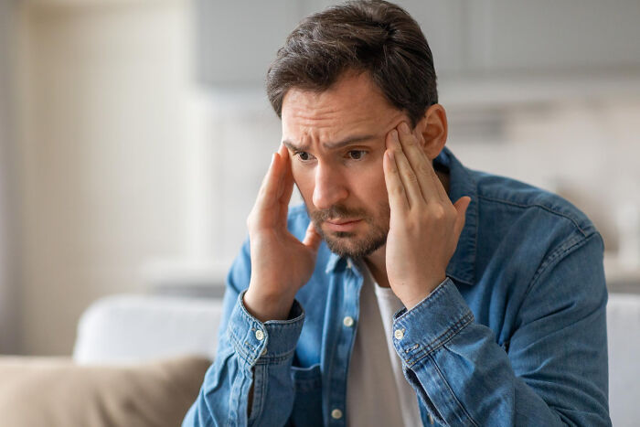 Man in a denim shirt experiencing a stressful moment, holding his head with both hands, reflecting on unexpected feelings.