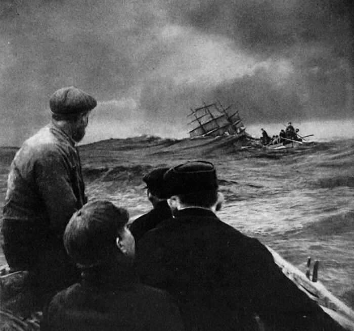 Men in a boat watching a distressed shipwreck on rough seas, illustrating the sad and sometimes horrific history of humanity.