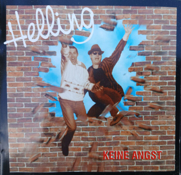 Hilariously bad album cover featuring two men jumping through a brick wall with playful expressions and casual clothing.