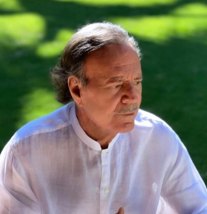 Julio Iglesias, Enrique Iglesias' famous father, pictured outdoors wearing a white shirt amid investigation and accusations.
