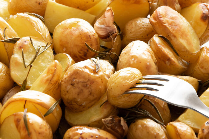 Close-up of roasted potatoes with rosemary and garlic, highlighting a fork picking up a crispy golden potato.