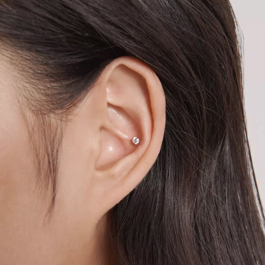 Close-up of a woman's ear featuring a daith ear piercing with a small clear gemstone stud earring.