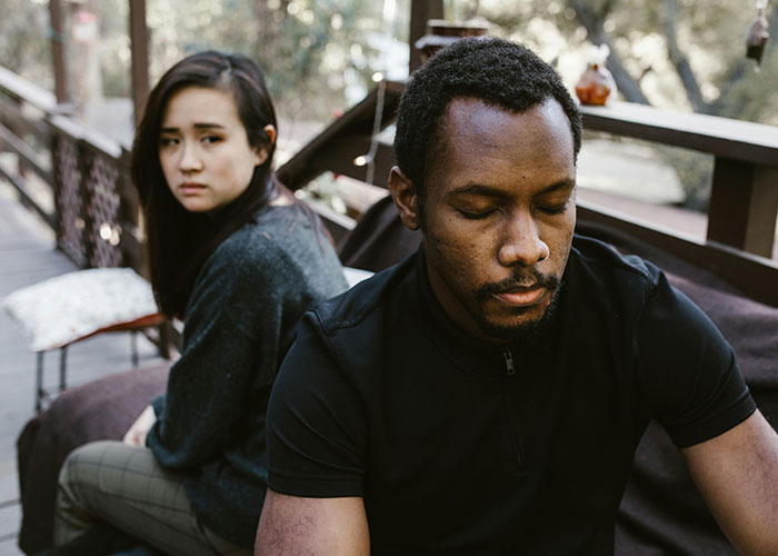 Couple sitting apart outdoors with tense expressions, capturing husband&rsquo;s weird behavior and wife&rsquo;s reaction at dinner.