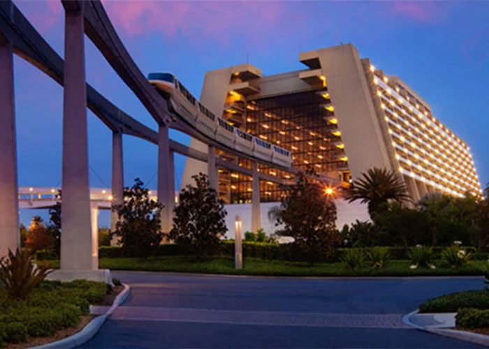 Disney World resort exterior at dusk with monorail passing, lit hotel facade and landscaping in foreground
