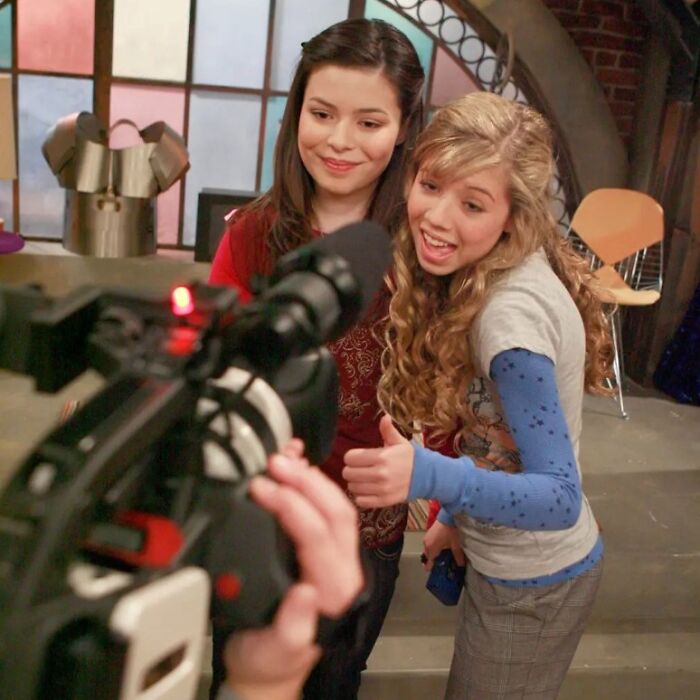 Two teenage girls smiling and posing on a TV set, illustrating twisted and addictive relationship themes.