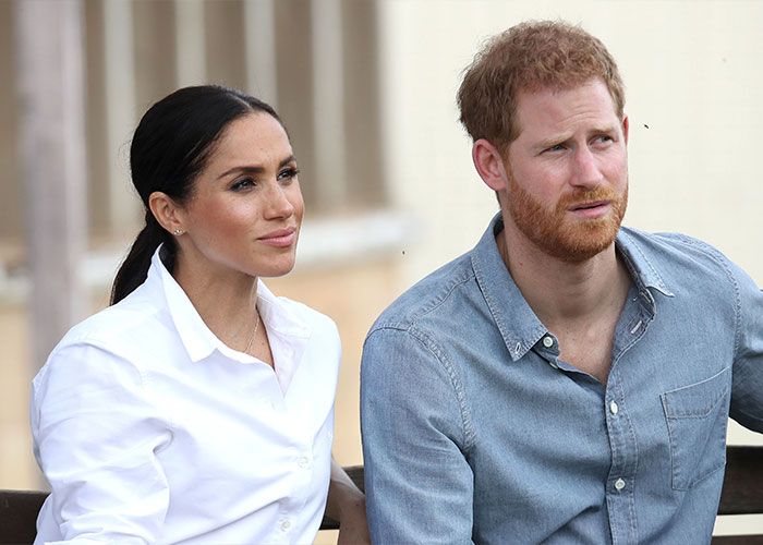 Meghan Markle and Prince Harry sitting together outdoors, highlighting Meghan Markle's family rift theories.