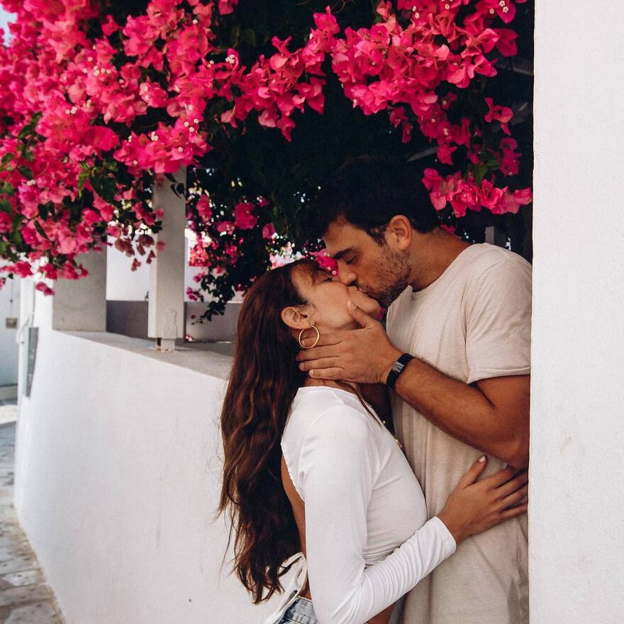 Couple sharing a romantic kiss beneath vibrant pink flowers, illustrating fun questions to ask your partner connection.