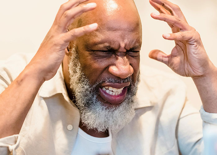 Frustrated man with gray beard raising hands in anger, illustrating intense emotions related to perfect revenge acts.