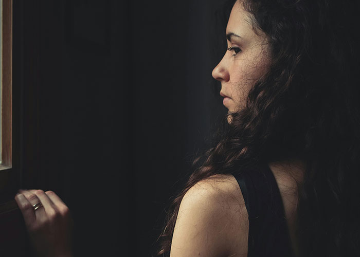 Woman with curly hair looking out window, reflecting on a romantic getaway situation involving friend and husband conflict.