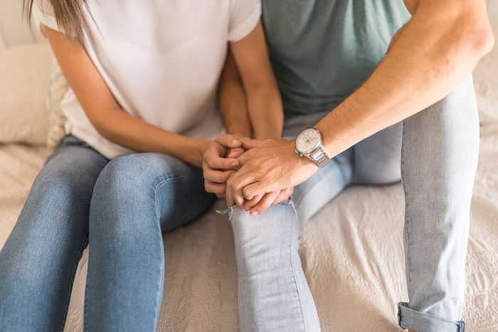 Young couple sitting on bed holding hands, suggesting boyfriend red flags and tension