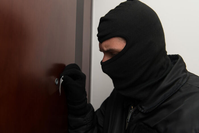 Masked man attempting to pick a door lock, illustrating security concerns women address to feel safer while living alone.