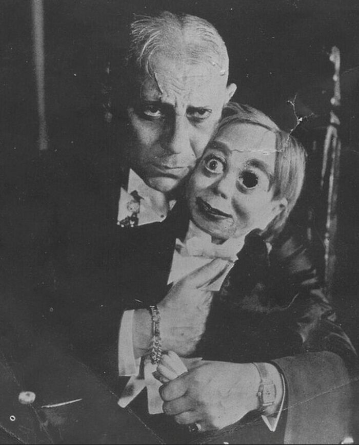 Black and white vintage photo of a man holding a creepy ventriloquist dummy with odd facial expressions.