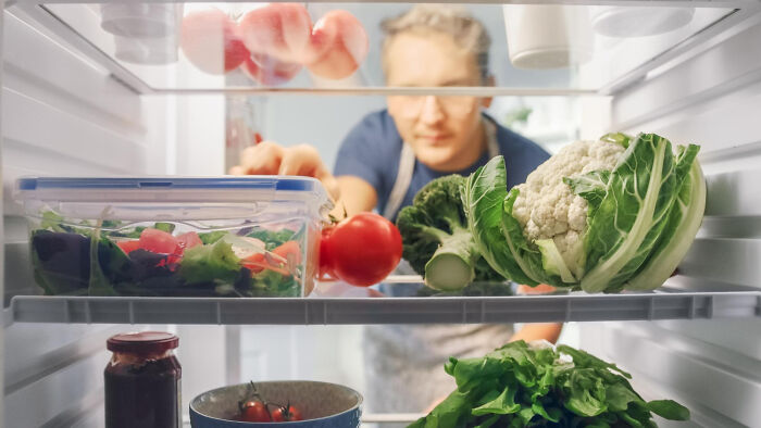 Person reaching into fridge filled with fresh vegetables and salad, illustrating weird iconic satisfying situations not my problem anymore