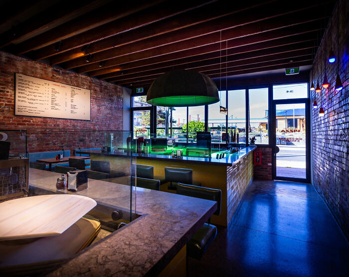 Interior of a modern pizzeria with brick walls and a menu board, related to a pizzeria owner and online reviews.