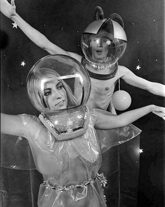 Two people in old black and white photo wearing odd and creepy space helmets and costumes with stars in the background.