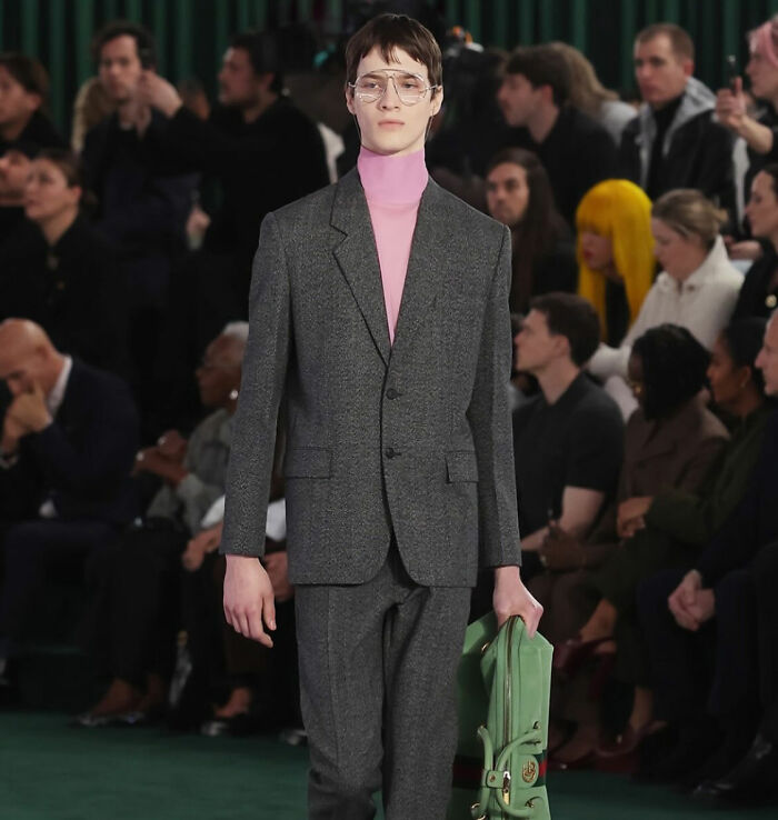 Male model in gray suit and pink turtleneck walking runway, featured in viral Gucci male models 1995 and 2025 comparison video