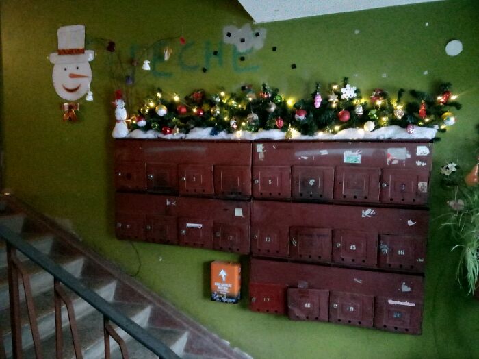 Christmas decorations with lights and ornaments on old mailboxes in a Lithuanian apartment building hallway.