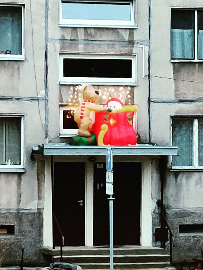 Inflatable Christmas decorations on a weathered Lithuanian apartment building balcony with holiday lights.