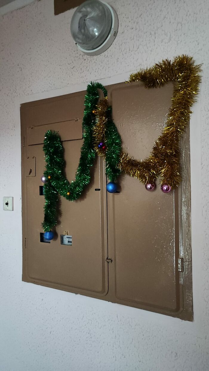 Green and gold tinsel with baubles awkwardly decorated on a plain utility panel in a Lithuanian apartment building.