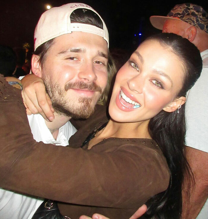 Brooklyn Beckham embraces a woman at a nighttime event amid rumors of a family feud involving his parents.