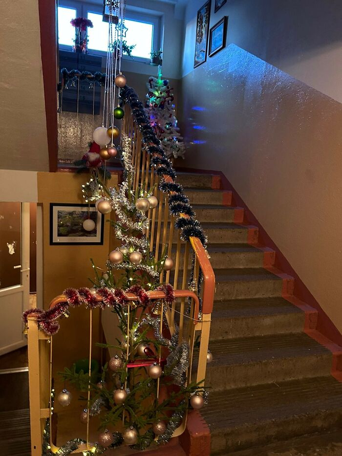Christmas decorations on a staircase in a Lithuanian apartment building featuring tinsel, lights, and ornaments in a sad setting.