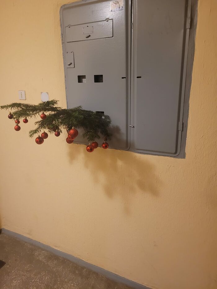 Spruce branch with red ornaments hanging from a gray electrical panel in a Lithuanian apartment Christmas decoration.