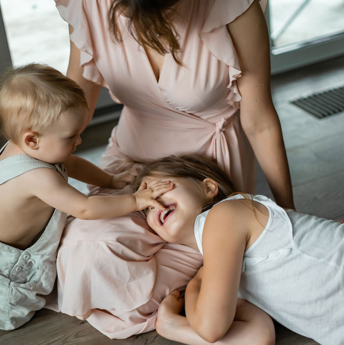 Mother with two children playing on floor, toddler covering girl's face, representing dating deal-breakers
